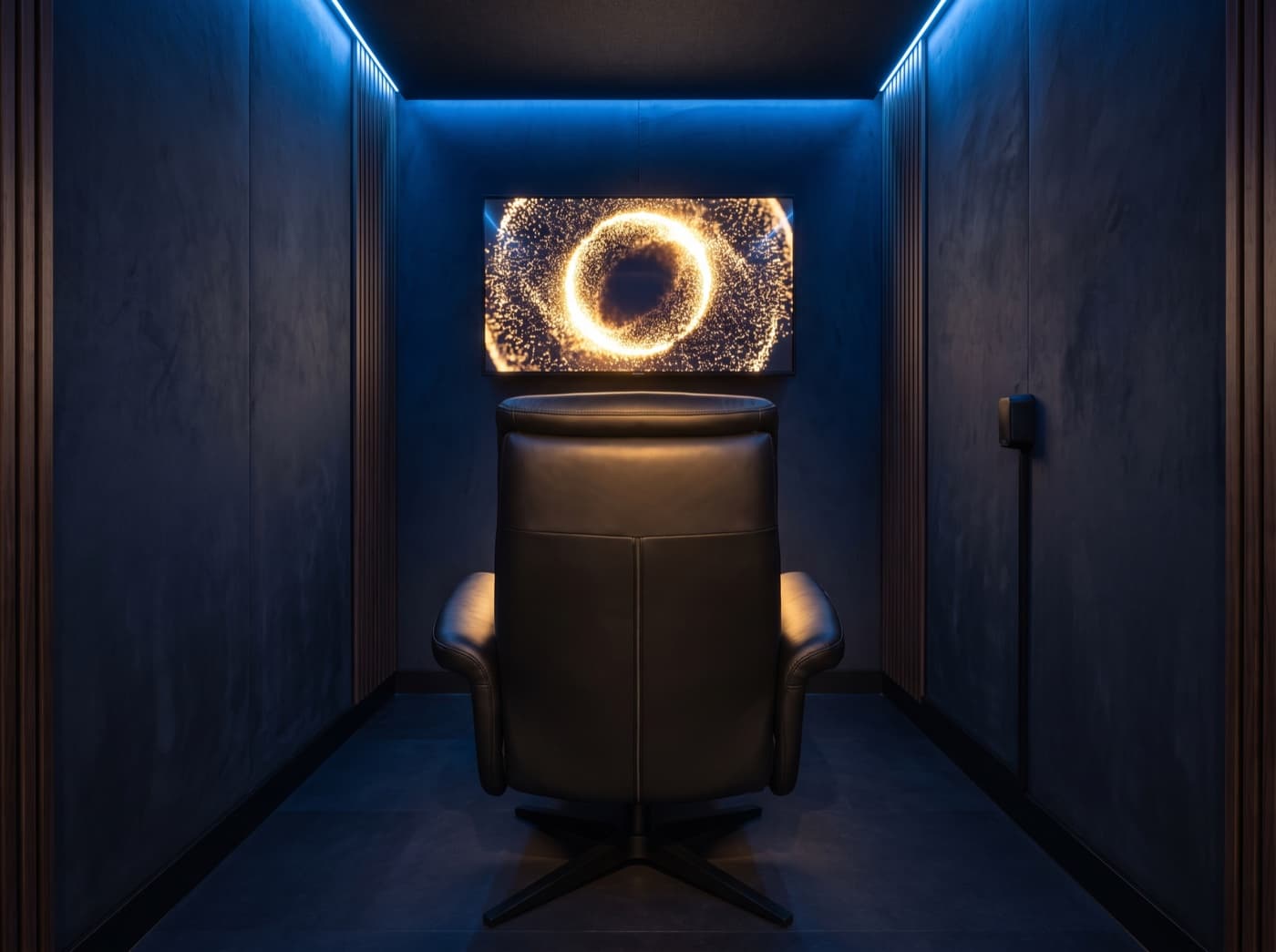 Interior do Recovery Pod visto de trás da poltrona: a poltrona reclinável de couro preto voltada para a tela onde brilha o globo luminoso da Alive, sob iluminação perimetral azul.